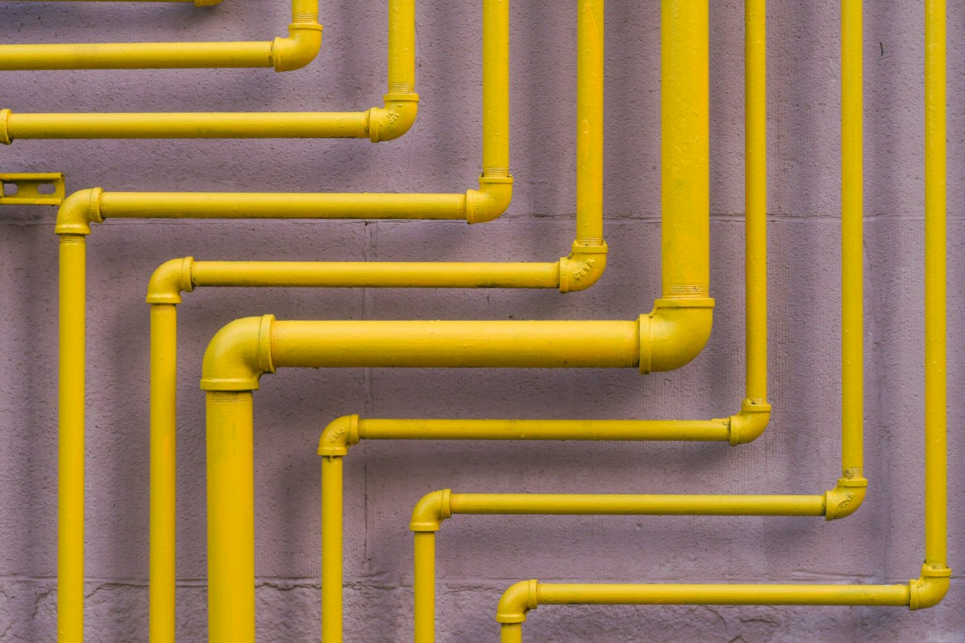 Bright yellow pipes zig-zagging across a lilac wall